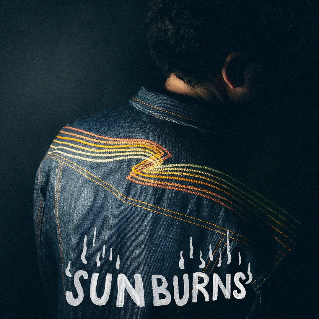 Rückansicht einer dunkelblauen Jeansjacke mit gelben Stickereien und dem Schriftzug SUNBURNS.