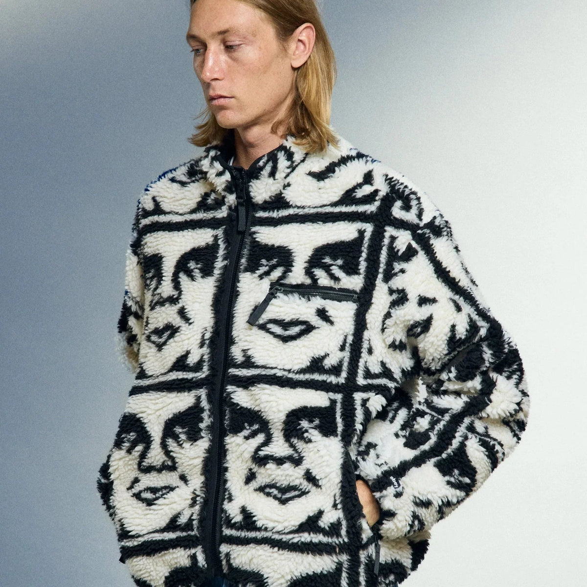Mann trägt eine schwarz-weiße Fleecejacke mit abstraktem Gesichtsmuster von Obey