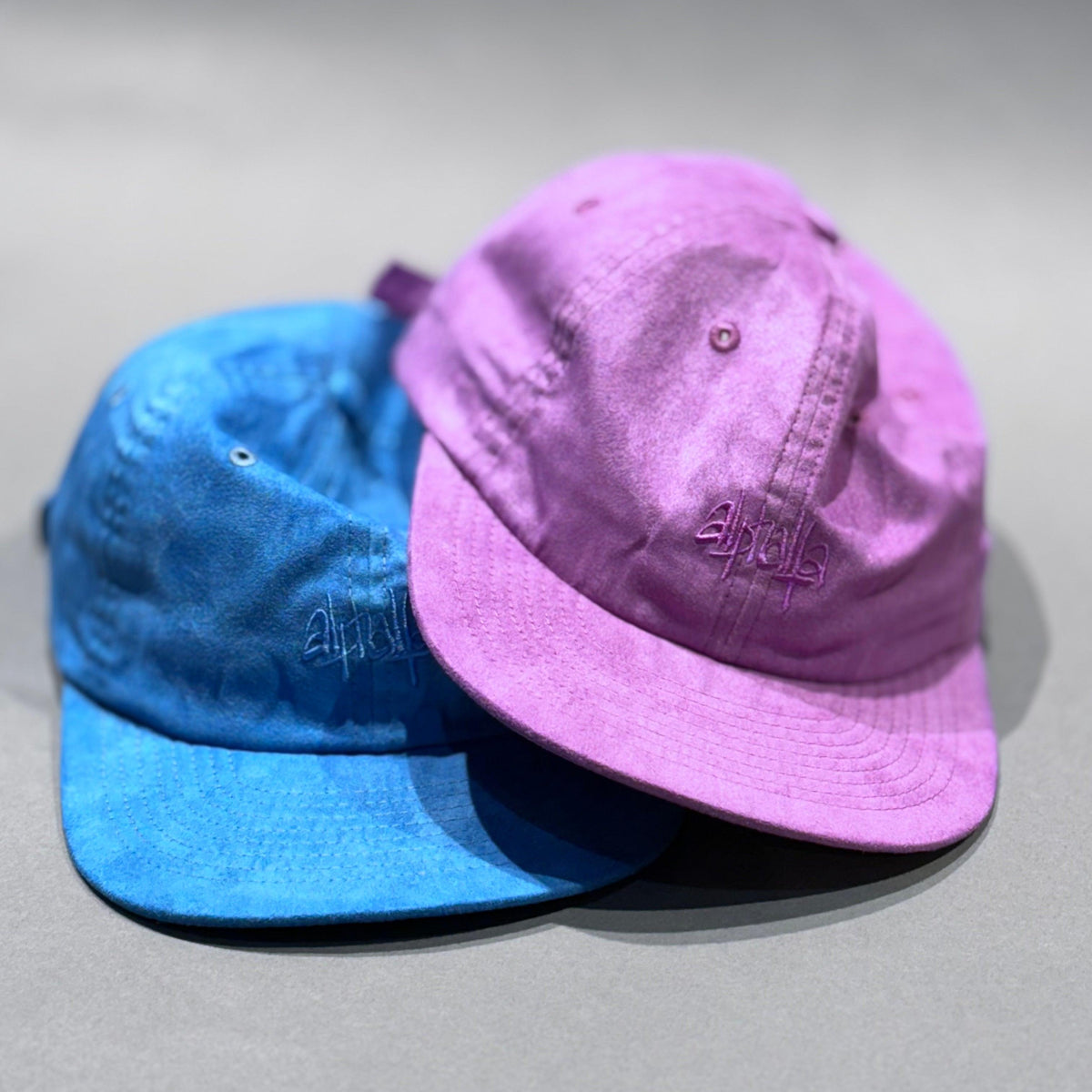 Zwei Alphalfa 6 Panel Caps in Blau und Lila, garment dyed, mit gesticktem Logo.