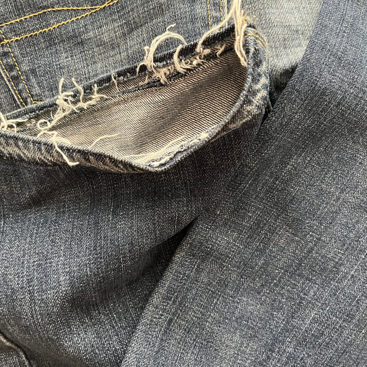 Detailaufnahme einer abgenutzten, ausgefransten Stelle an einer blauen Denim-Jeans