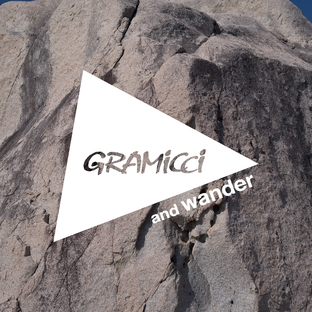 Gramicci und and wander Logo auf einer grauen Felswand vor blauem Himmel