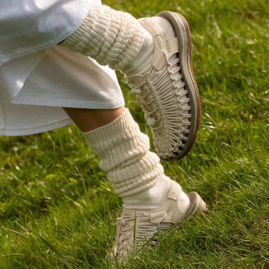 Nahaufnahme von beigen Keen Outdoor-Schuhen mit gestrickten Socken im grünen Gras