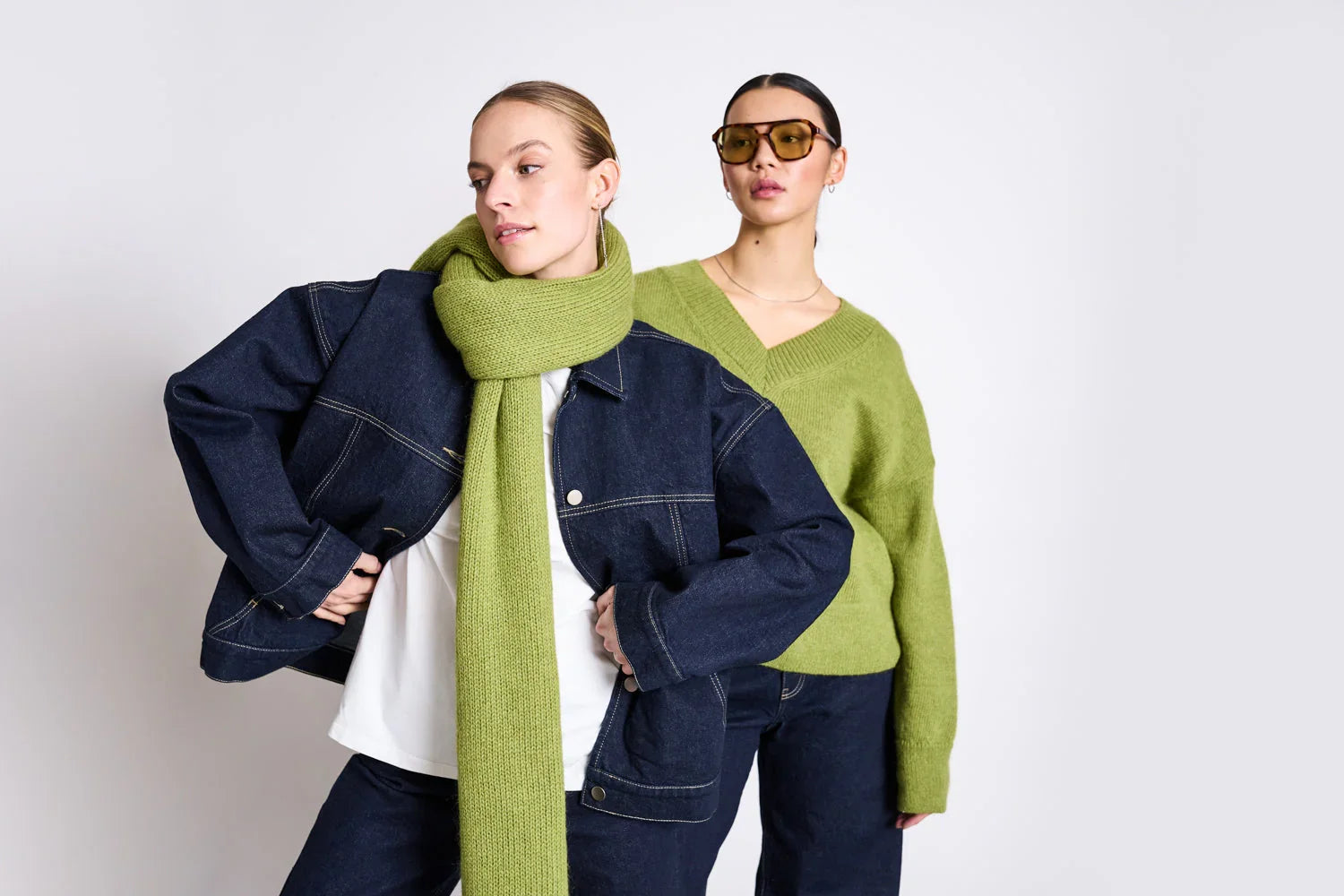 Zwei Frauen in herbstlicher Mode mit dunkelblauer Jeansjacke, grünem Strickpullover und Schal.