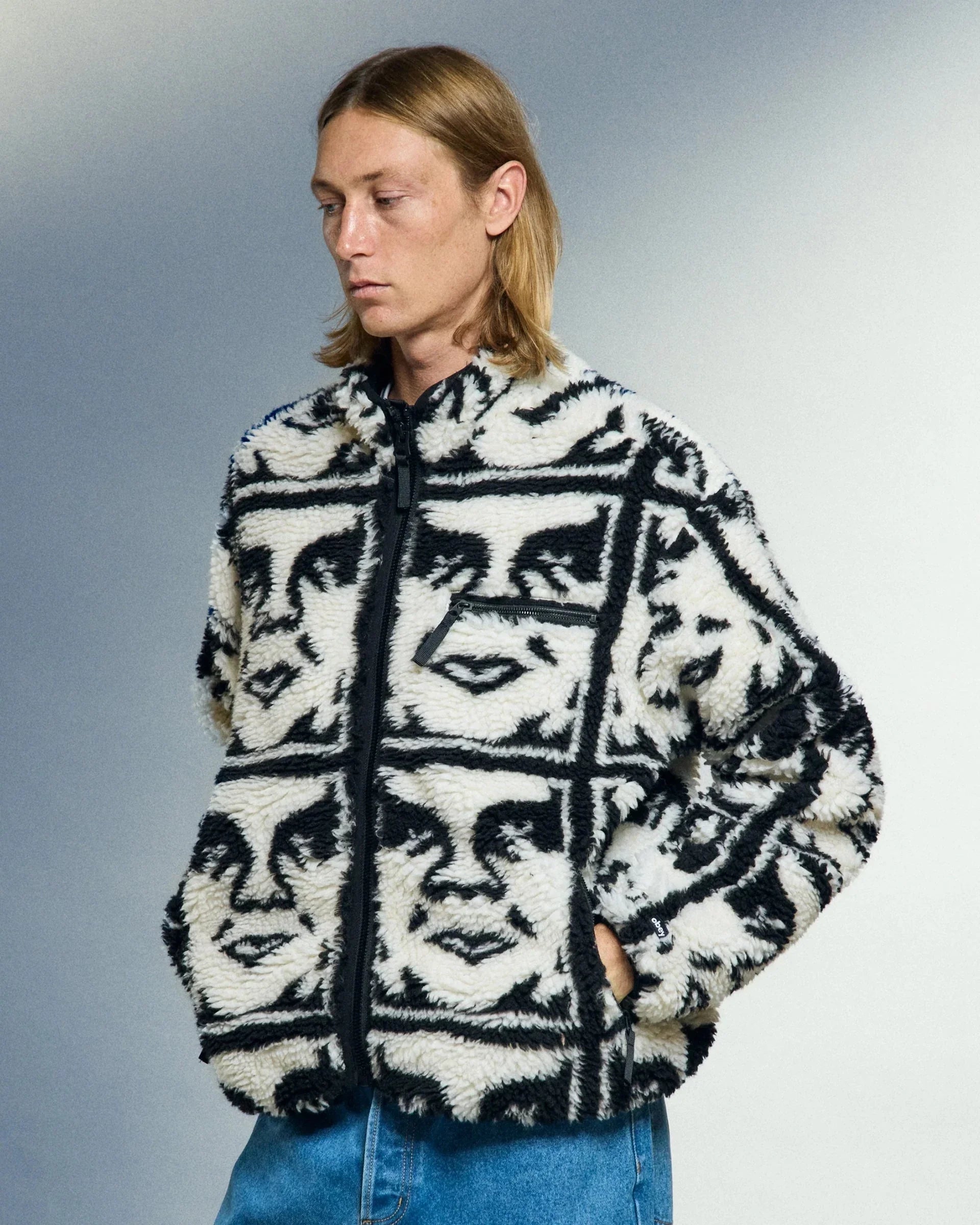 Mann trägt eine schwarz-weiße Fleecejacke mit abstraktem Gesichtsmuster von Obey