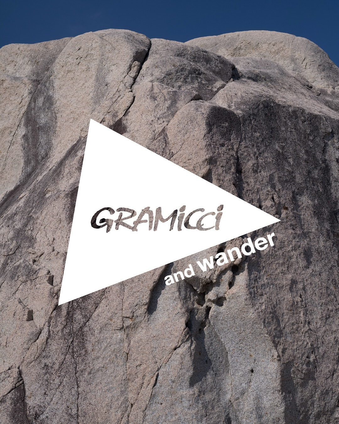 Gramicci und and wander Logo auf einer grauen Felswand vor blauem Himmel