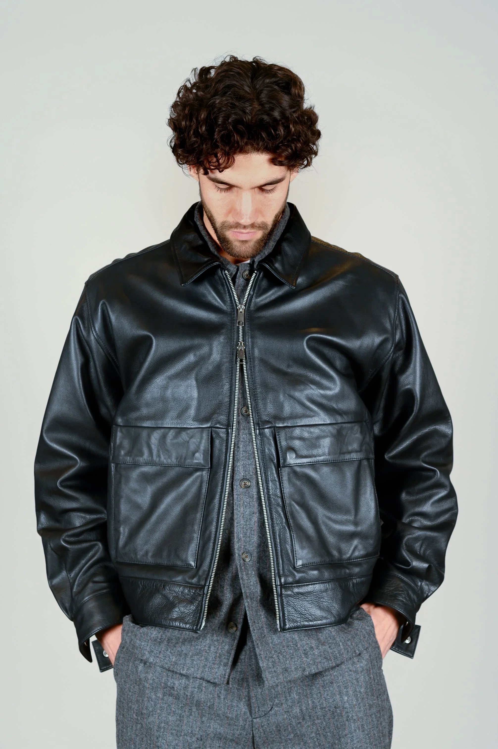 Mann in schwarzer Lederjacke und grauer Stoffhose aus dem Herbst/Winter Lookbook.