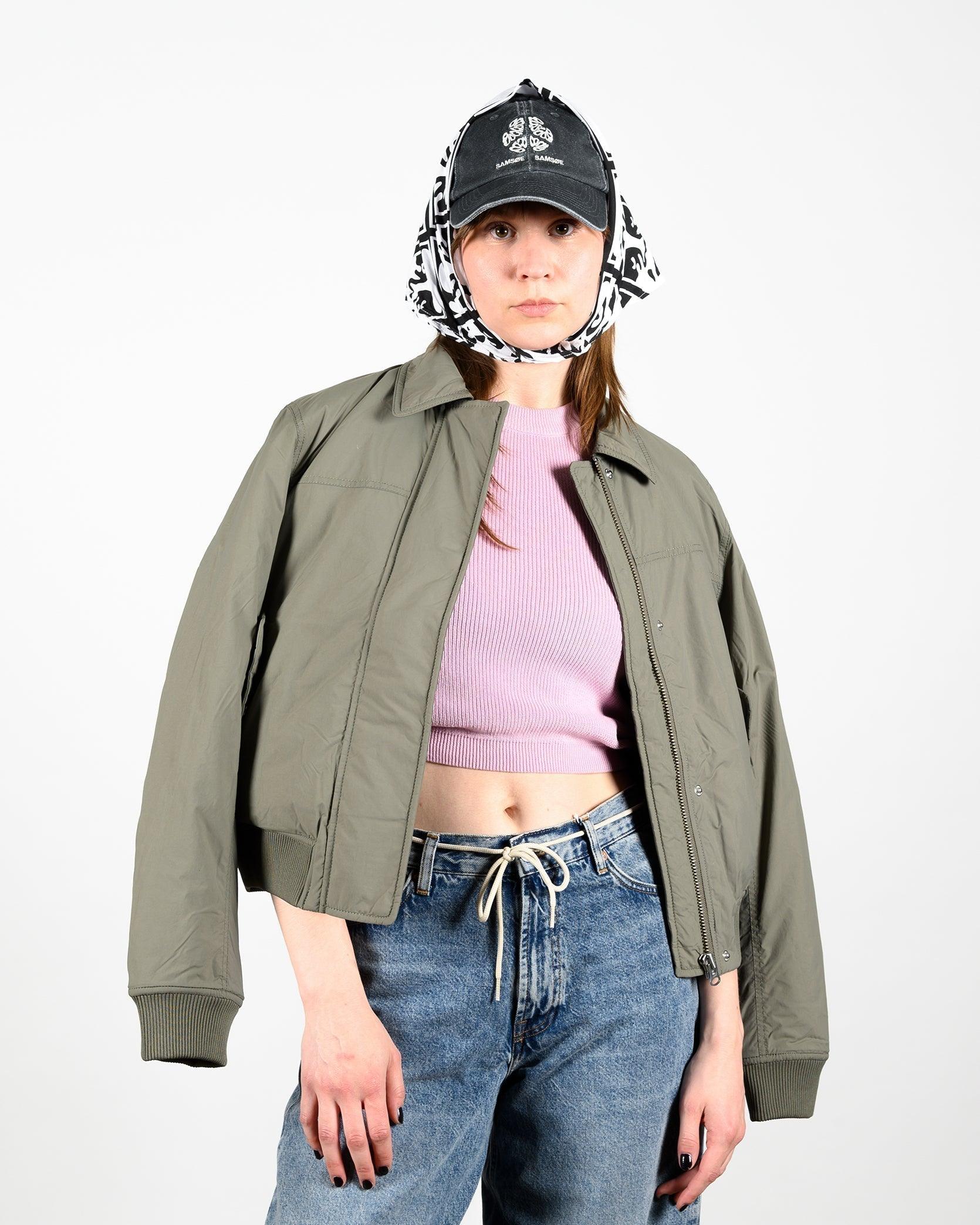 Frau im Frühlingslook mit khakifarbener Jacke, rosa Crop-Top, Jeans und gemusterter Kopfbedeckung