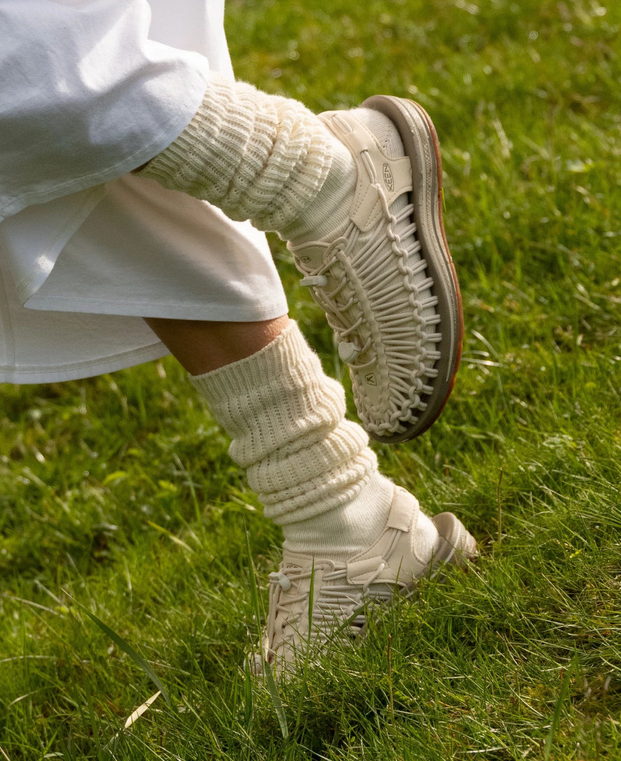 Nahaufnahme von beigen Keen Outdoor-Schuhen mit gestrickten Socken im grünen Gras
